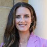 A woman with long brown hair, wearing a Howard Payne University purple blazer and a cross necklace, smiling at the camera. | HPU